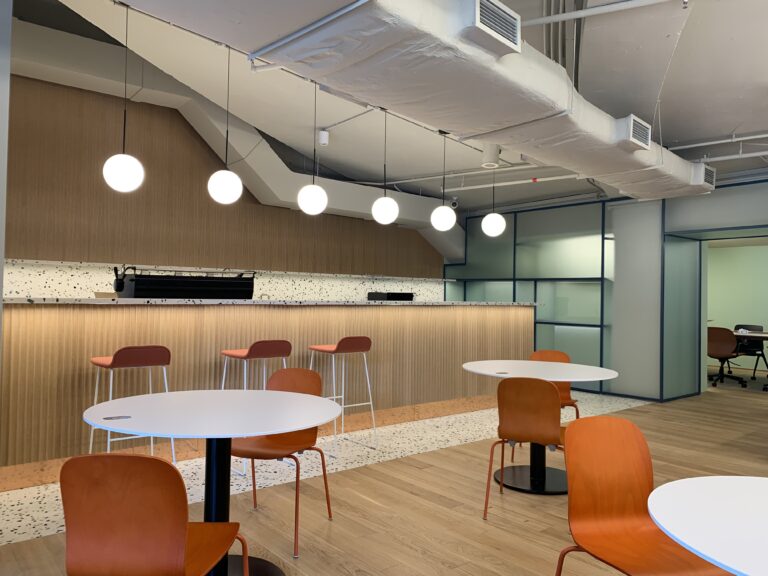 A contemporary modern interior fit-out for a coworking space featuring orange wood-tone chairs and feature lights overhung on the kitchen area