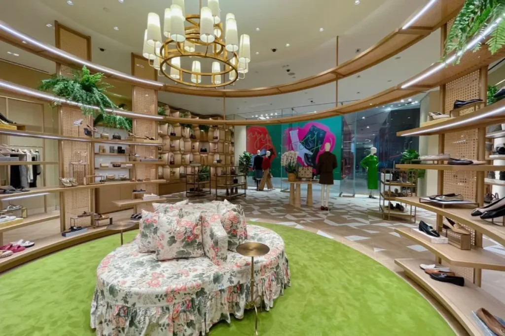 Tory Burch boutique interior at Siam Paragon with curved shelving, floral seating, green carpet, and warm lighting.