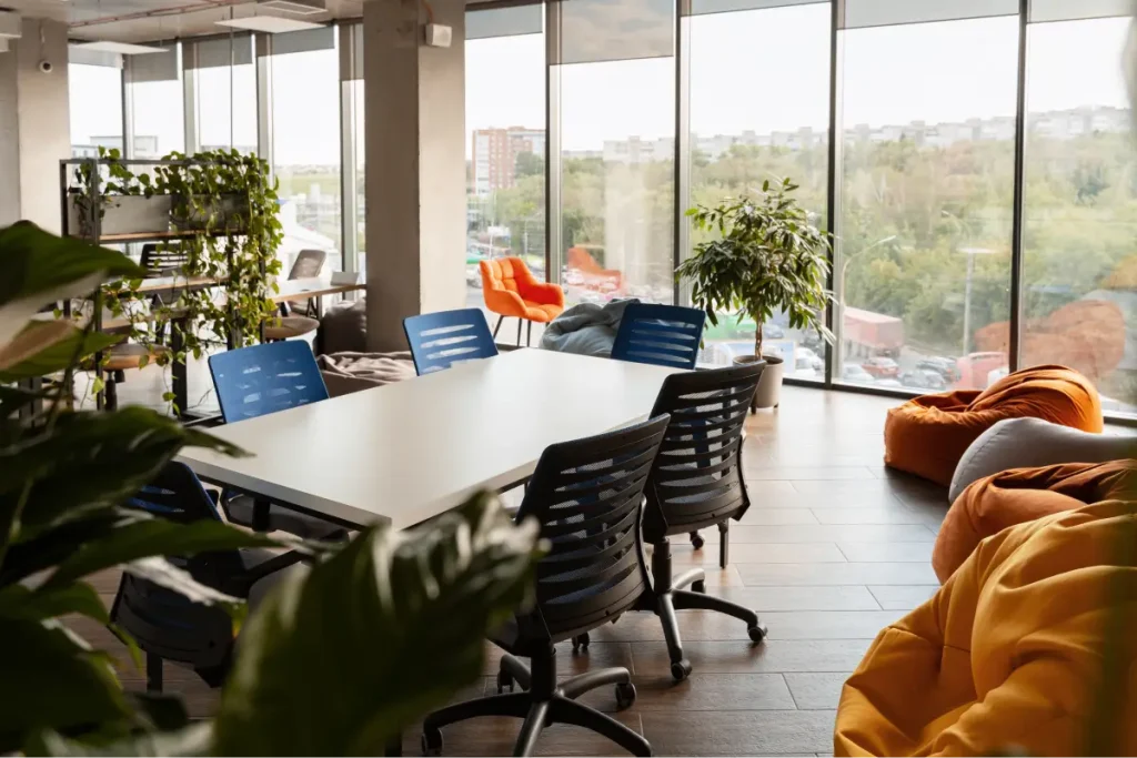 Office table with chairs in a room filled with plants, earth-toned furniture, and large windows