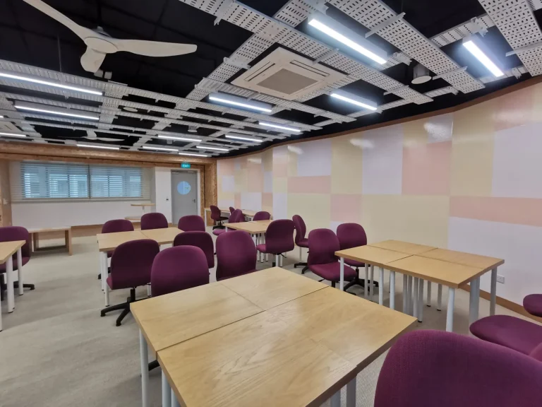 An office space refurbish featuring maroon chairs, beige walls, and wooden tables built by an office refurbishment contractor